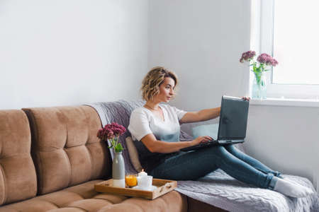 the programmer girl is sitting on a comfortable sofa in her home and working remotely on a laptop in a cozy environment.の写真素材