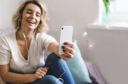 a young girl blogger leads an online broadcast communicates with her subscribers sitting at home on the couch in a cozy atmosphereの写真素材