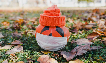 two pumpkin the healthy and the sick.Pumpkin in a mask and a knitted cap of orange color on multi-colored autumn leaves.の写真素材