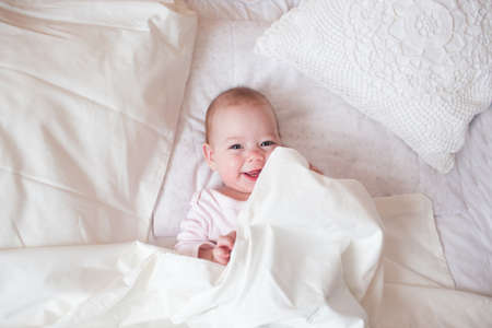 the child is lying in a cozy bed and laughing. The kid saw his mother.の写真素材