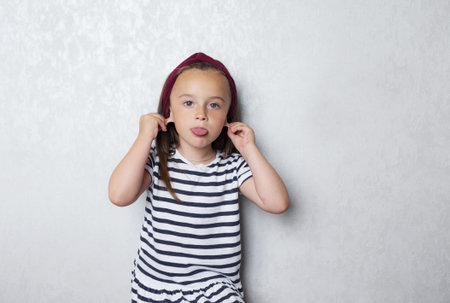 a little girl in a striped t-shirt with black and white stripes stands against the wall and makes...