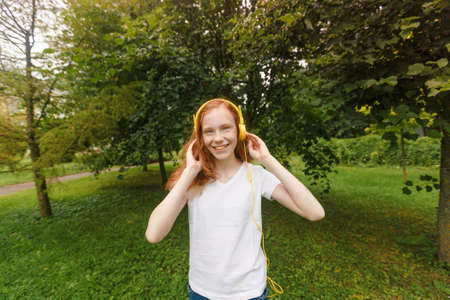 red-haired girl listens to lessons with headphones. Lying on the grassの写真素材