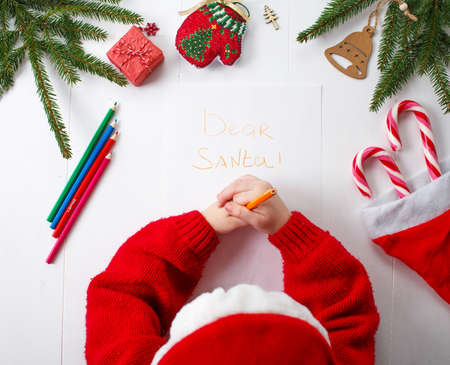 A little girl in a red Christmas hat writes a letter to Santa Clausの写真素材