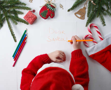 A little girl in a red Christmas hat writes a letter to Santa Clausの写真素材