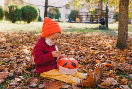 a little girl in a red sweater sits on the autumn grass in the Park and gives an injection to a sick pumpkin COVID19.の写真素材