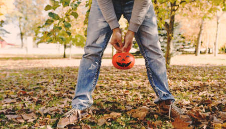 a man in blue jeans holds a pumpkin between his legs in a Park among yellow leaves.の写真素材