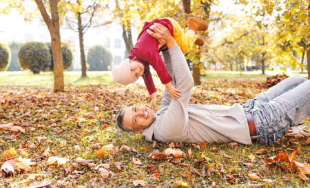 happy dad plays with his little daughter in the Park on autumn leaves lifts her high in his armsの写真素材