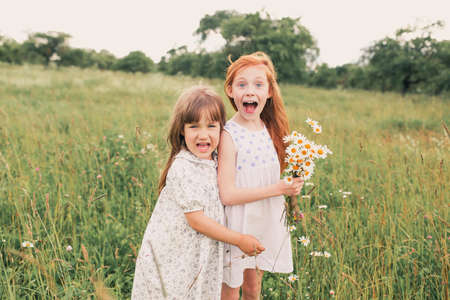 two little girls sisters play and have fun on the grass holding hands in light dresses.Summer, Sunny weather in a good mood.の写真素材