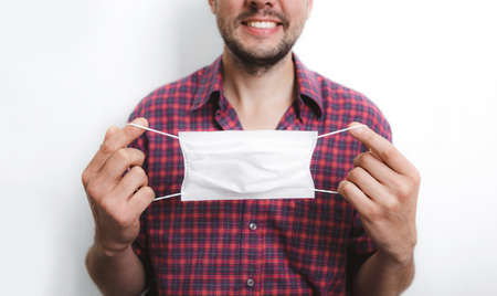 a man in a red checked shirt wears a medical mask against a white wall.の写真素材