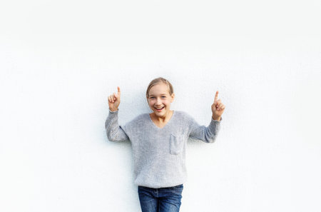 a girl in a gray sweater poses against a white wall.