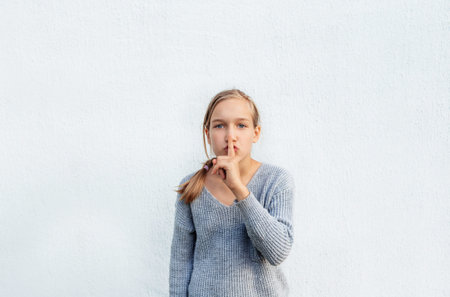 a girl in a gray sweater poses against a white wall.