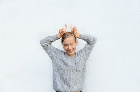 a girl in a gray sweater poses against a white wall.