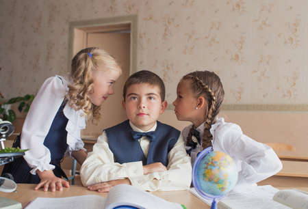 two girls and a boy at school at a Desk studying biology and geography, discussing homework.の写真素材