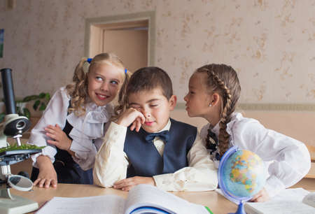two girls and a boy at school at a Desk studying biology and geography, discussing homework.の写真素材