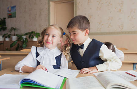 two students a boy and a girl sit at a Desk at school and communicate with each other in the ear.の写真素材
