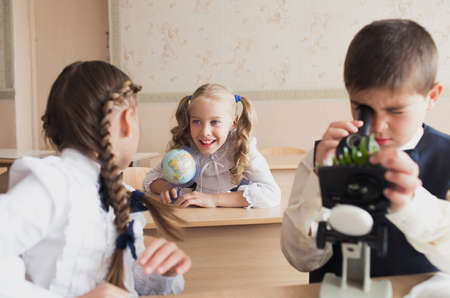 two girls and a boy at school at a Desk studying biology looking through a microscope science and biology at schoolの写真素材