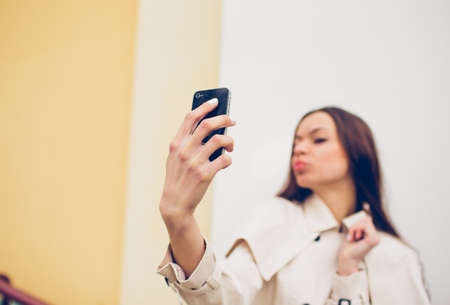 beautiful young girl in a light raincoat takes a selfie on her phone.の写真素材