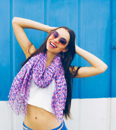 a young girl in large round glasses stands against a blue wall.の写真素材