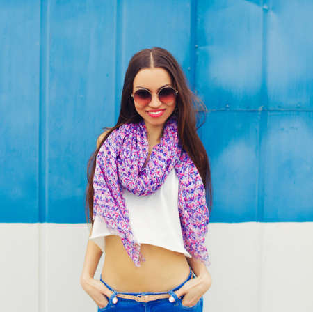 a young girl in large round glasses stands against a blue wall.の写真素材