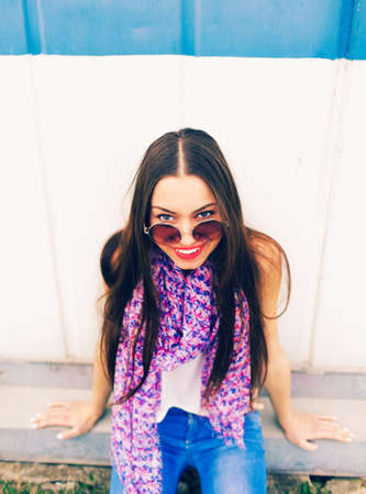 a young girl in large round glasses stands against a blue wall.の写真素材