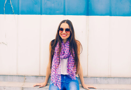 a young girl in large round glasses stands against a blue wall.
