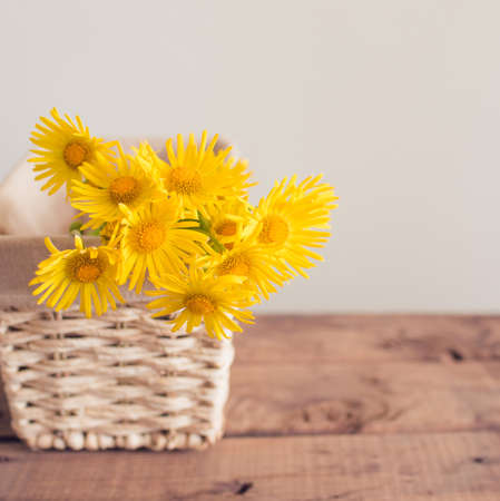 Bouquet of yellow flowers in a basket on a wooden backgroundの写真素材