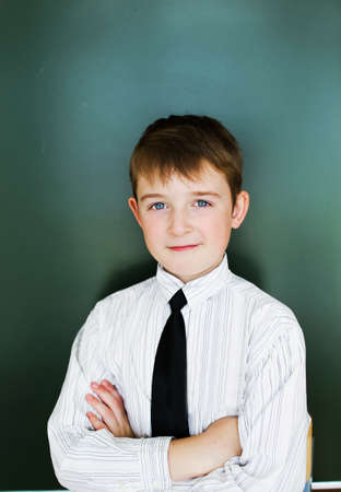 A schoolboy boy stands near the blackboard in a white shirt and tieの写真素材