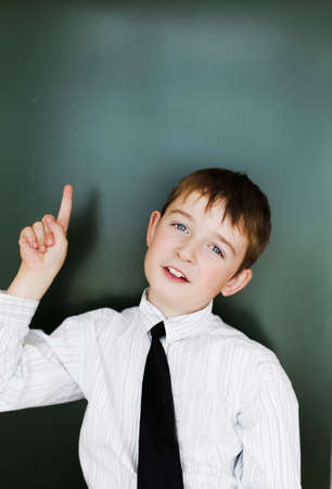 A schoolboy boy stands near the blackboard in a white shirt and tieの写真素材