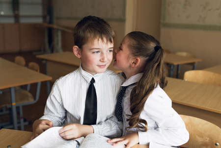 a boy and a girl students sit at a Desk and talk in each others earの写真素材