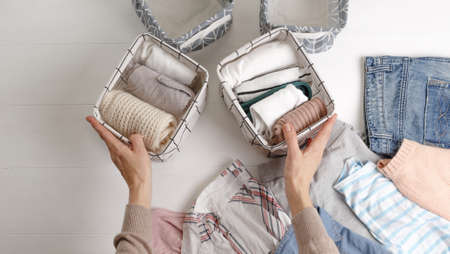 The woman carefully folds the clothes and puts them in baskets and boxes. Minimalism in the Scandinavian style.の写真素材