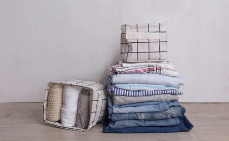 A stack of colorful, perfectly folded items of clothing. A bunch of different pastel shirts, sweaters and other items of clothing on a white background. Baskets for clothes storage.の写真素材