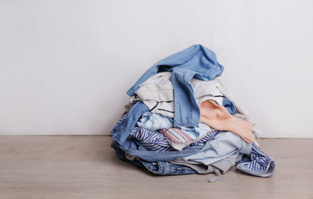 a pile of dirty multicolored clothes prepared for washing is lying on the floor in the light backgroundの写真素材