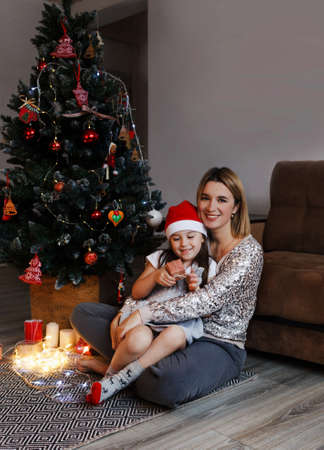 concept of family, Christmas, holidays and people-happy mother and little daughter sitting at home on the couchの写真素材