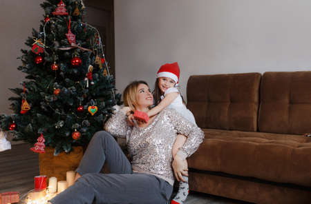 concept of family, Christmas, holidays and people-happy mother and little daughter sitting at home on the couchの写真素材