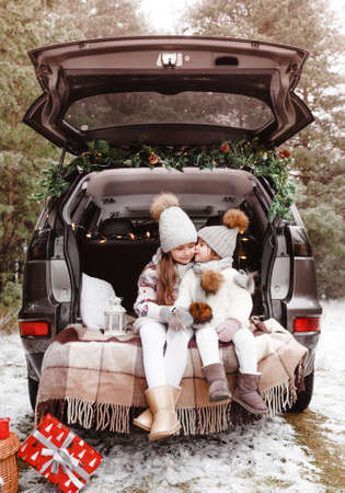 preparation for Christmas. Two little girls enjoy Christmas sitting in the trunk of a car. Cold winter, snowy weather.の写真素材