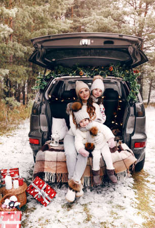 preparation for Christmas. Two little girls with their mother have fun playing in the trunk of a car. Cold winter, snowy weather.の写真素材