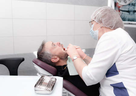 A female dentist treats the teeth of a male patient in the office of a dental clinic.Concept of medicine, dentistry and healthcare. Dental equipmentの写真素材
