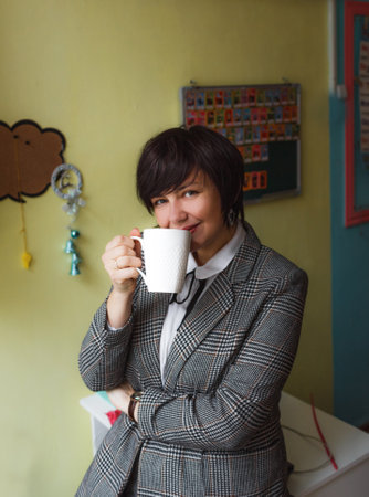 a girl teacher stands in the classroom and drinks tea in the absence of studentsの写真素材