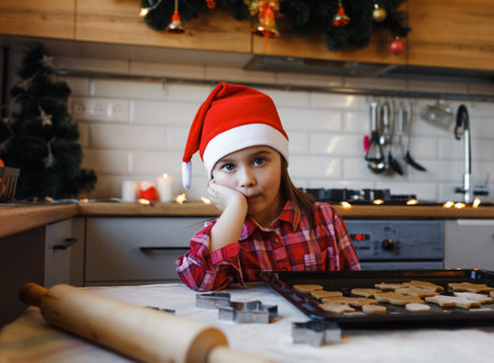 a little girl is sad in the kitchen near a tray of cookiesの写真素材