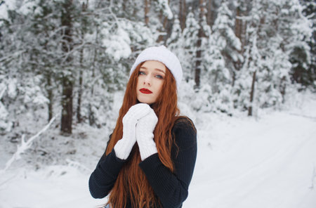 Young red-haired girl with long red hair on a winter background.Red-haired woman in a white hat on the background of winter nature.の写真素材
