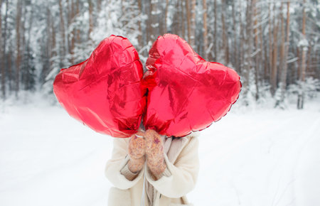 A young girl with a bright heart - shaped balloon is standing in a snowy forest. Valentines Dayの写真素材