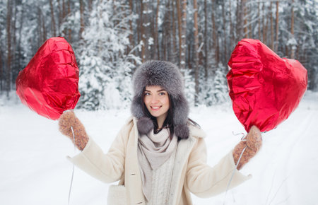 Portrait of a young girl with a bright heart-shaped balloon in a snow-covered forest. Valentines Dayの写真素材