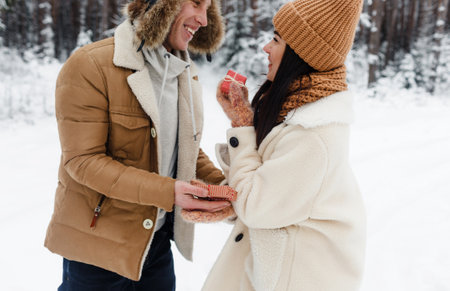 a guy gives a gift to a girl in a snow-covered forest. Surprise for Valentines Dayの写真素材