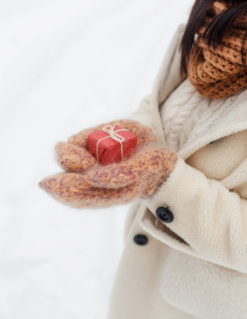 A young happy girl holds a gift box in her mittens in a snow-covered forest. Valentines Day.の写真素材