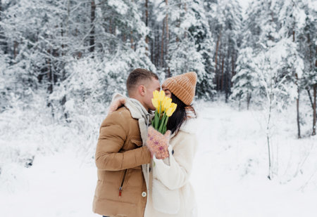 A young guy gives a bouquet of yellow tulips to a girl in a snowy forest. Valentines Day.の写真素材