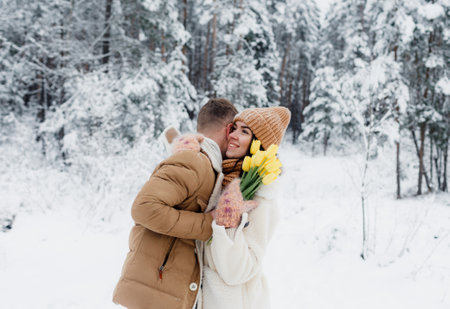 A young guy gives a bouquet of yellow tulips to a girl in a snowy forest. Valentines Day.の写真素材