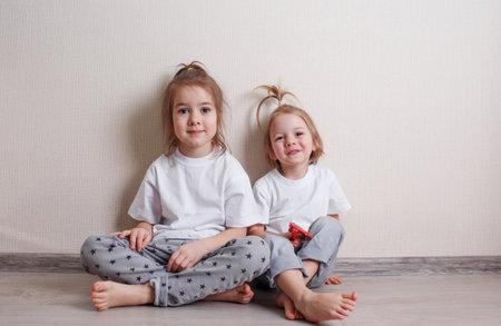 two little girls sit at home on the floor near the wall and laugh merrily.の写真素材