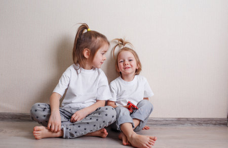 two little girls sit at home on the floor near the wall and laugh merrily.の写真素材