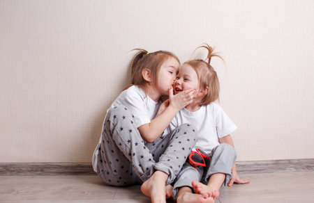 two little girls sit at home on the floor near the wall and play fun with each other. A fun and carefree childhood.の写真素材