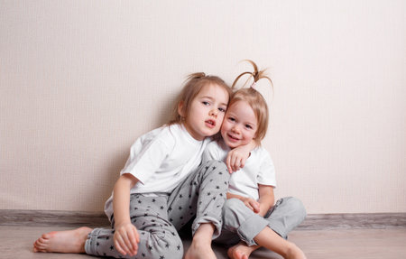 two little girls sit at home on the floor near the wall and play fun with each other. A fun and carefree childhood.の写真素材